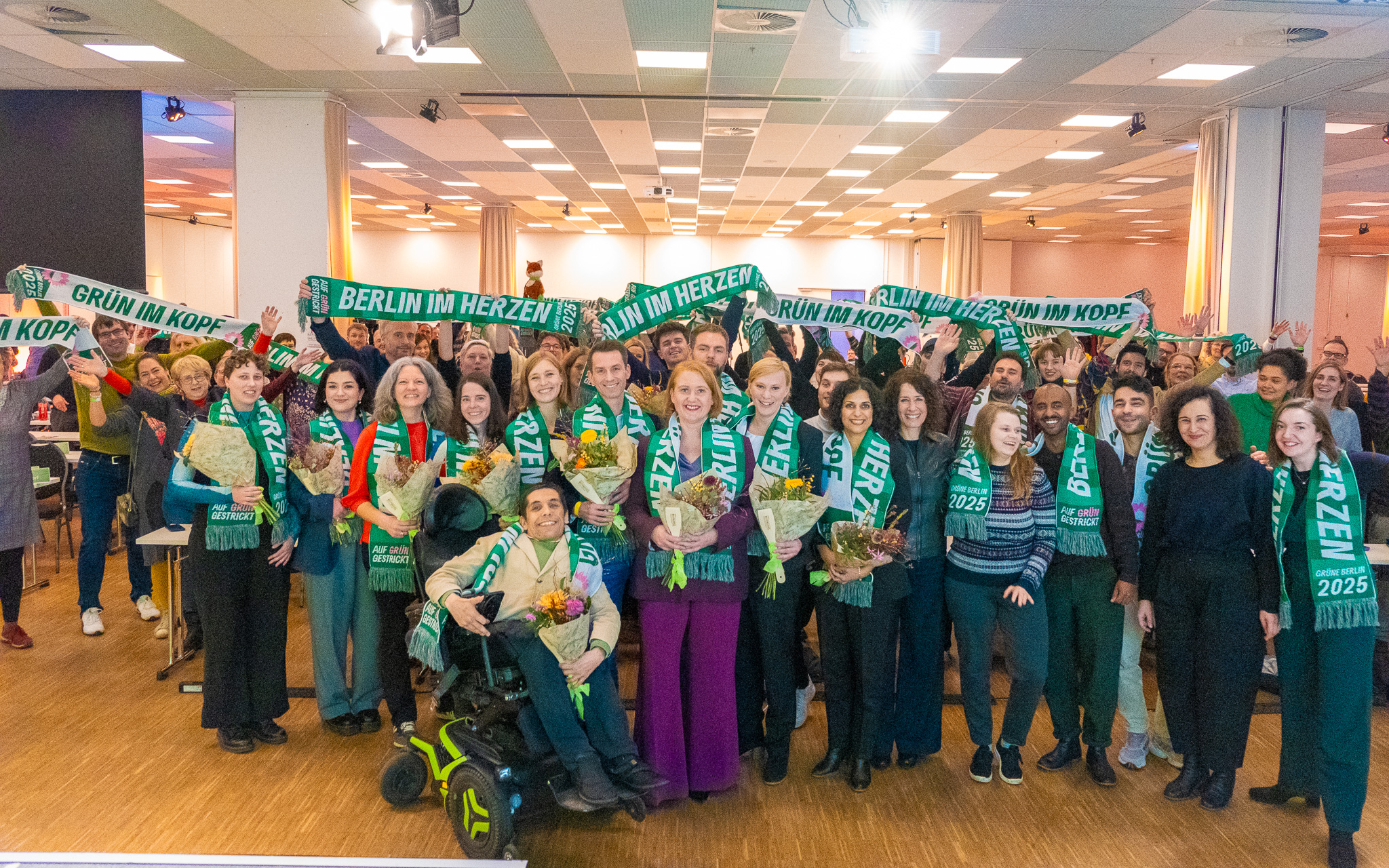 Gruppenfoto von der Landesdelegiertenkonferenz, im Vordergrund die 14 Kandidierenden auf der Landesliste zur Bundestagswahl. Alle tragen grüne Schals. Foto: Bündnis 90/Die Grünen Berlin