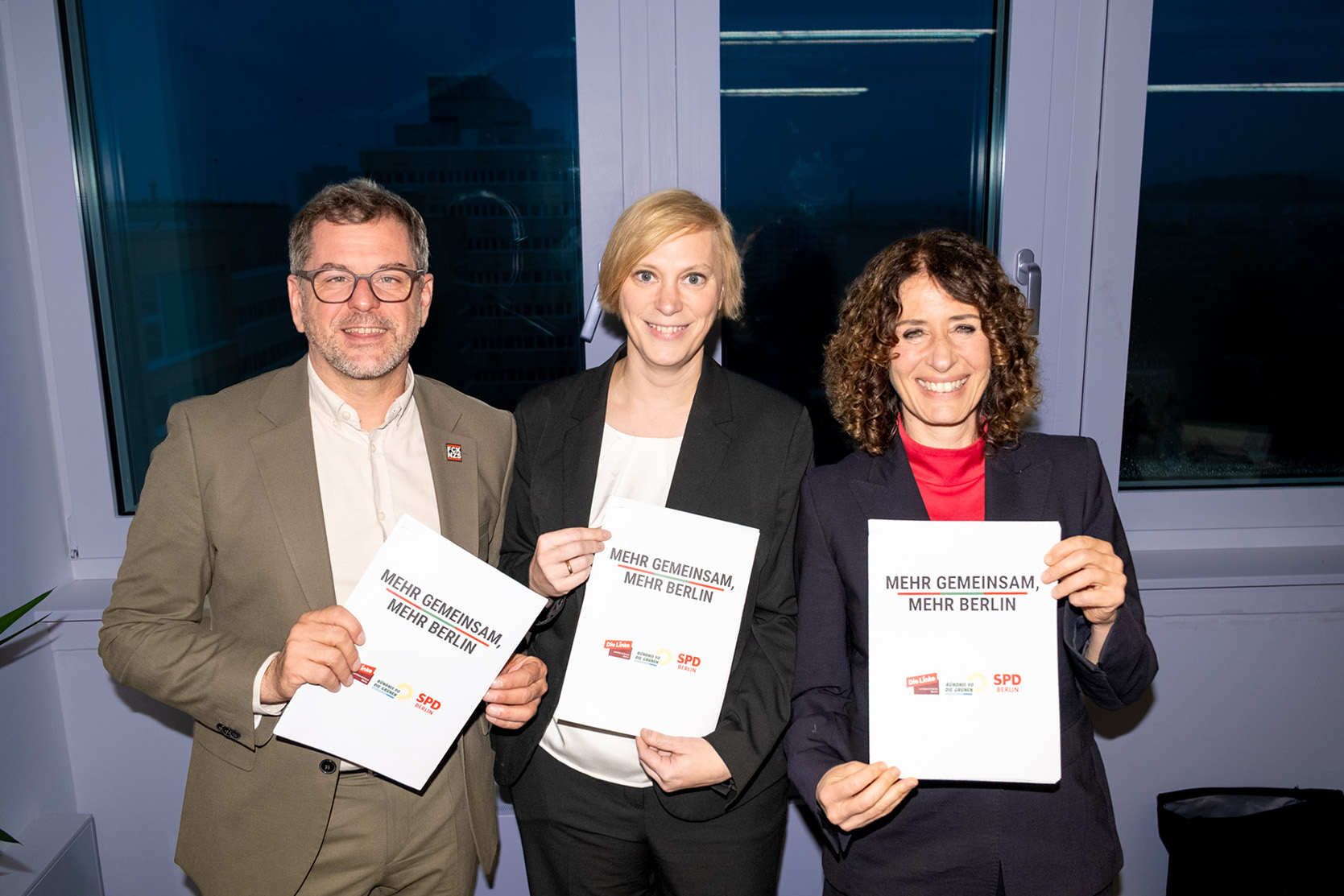 Werner Graf, Nina Stahr und Bettina Jarasch stehen nebeneinander und halten das Sondierungspapier in der Hand.