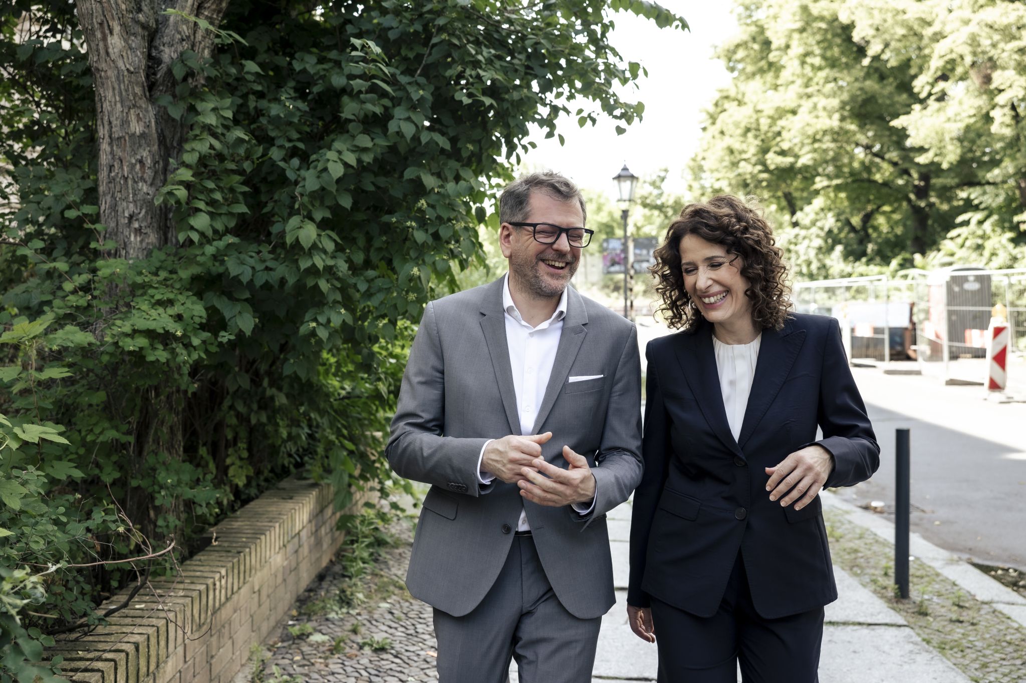 Werner Graf und Bettina Jarasch gehen eine Straße entlang, sie wenden sich einander zu und lachen sich an. Foto: Vincent Villwock