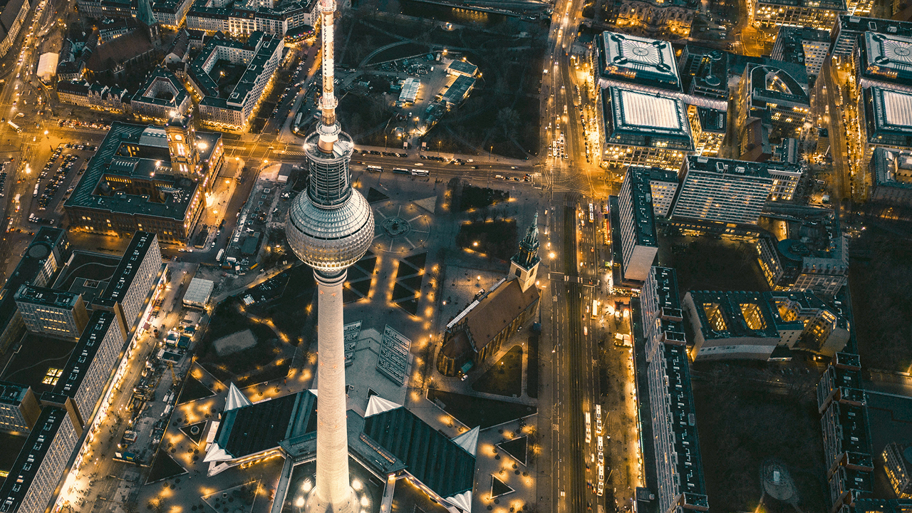 Eine Luftaufnahme von Berlin bei Nacht, zu sehen ist der Fernsehturm und das Rote Rathaus von oben umgeben von beleuchteten Straßen 