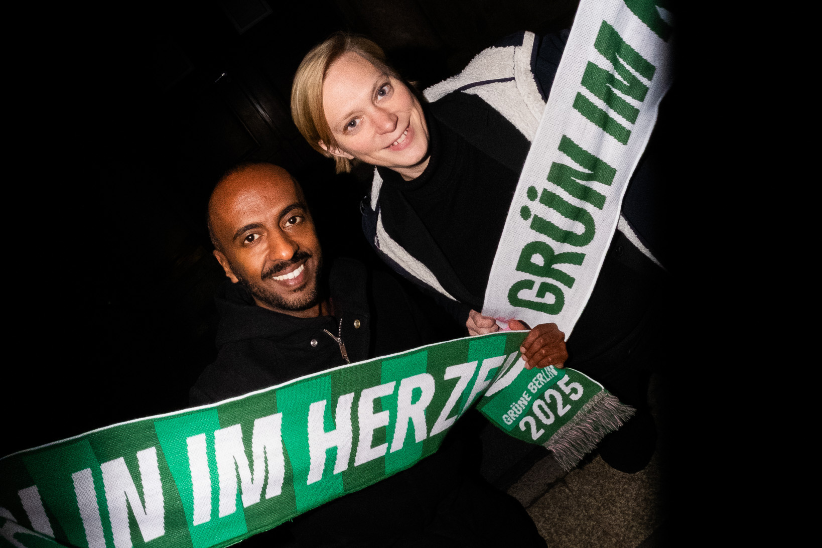 Philmon Ghirmai und Nina Stahr, Landesvorsitzende von Bündnis 90/Die Grünen Berlin, halten jeweils einen Schal in die Kamera. Auf den Schals steht "Berlin im Herzen" und "Grün im Kopf"