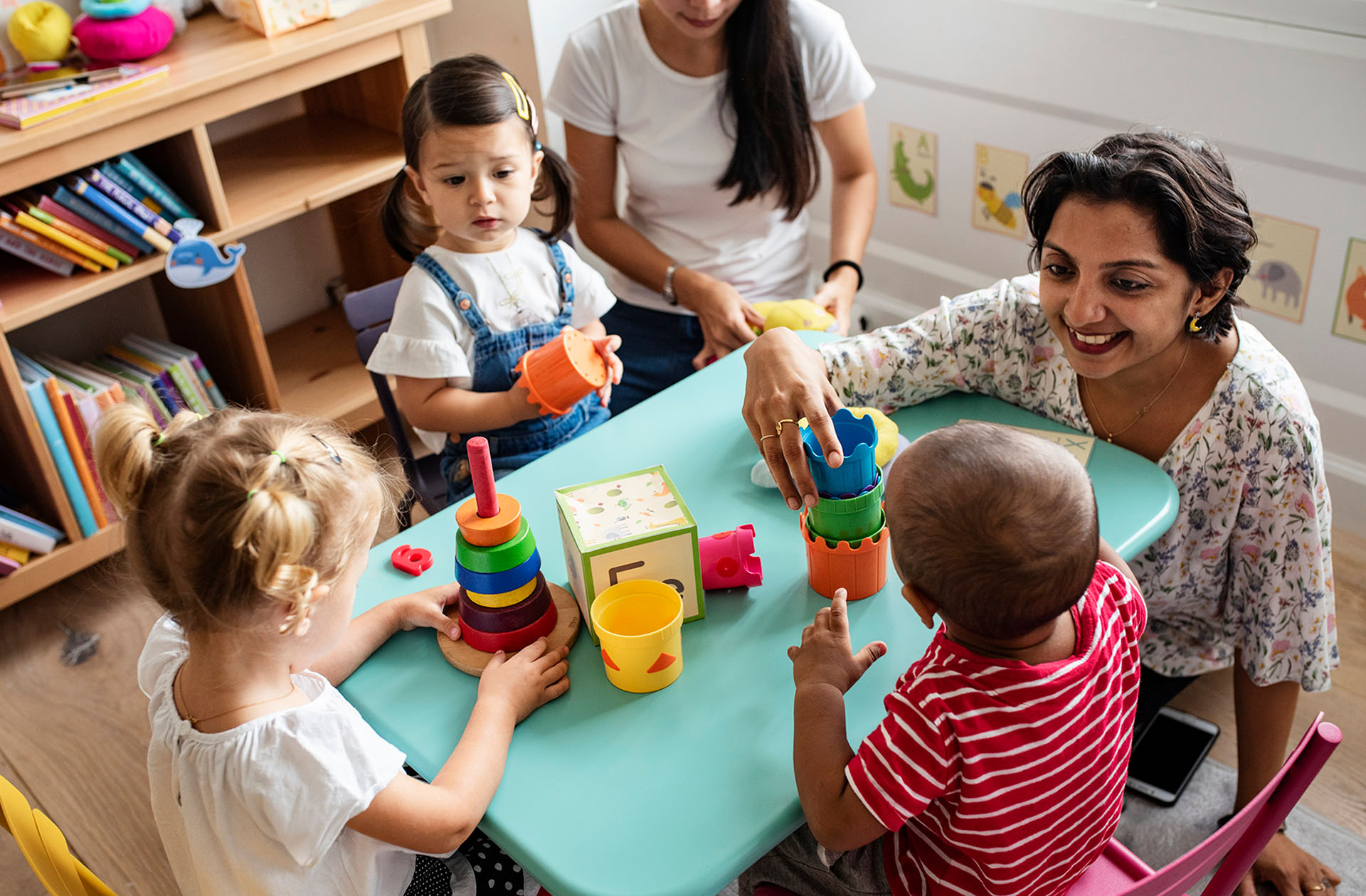 Eine Erzieherin in einer Kita, sie sitzt mit mehreren Kindern an einem Tisch und spielt mit ihnen.  Foto: Rawpixel via Getty Images&nbsp;