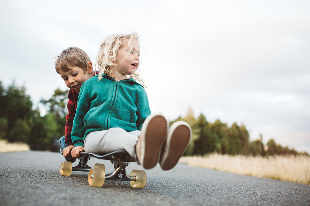 Zwei Kinder sitzen hintereinander auf einem Skateboard und rollen eine Straße entlang Foto: GettyImages/Ryan J. Lane