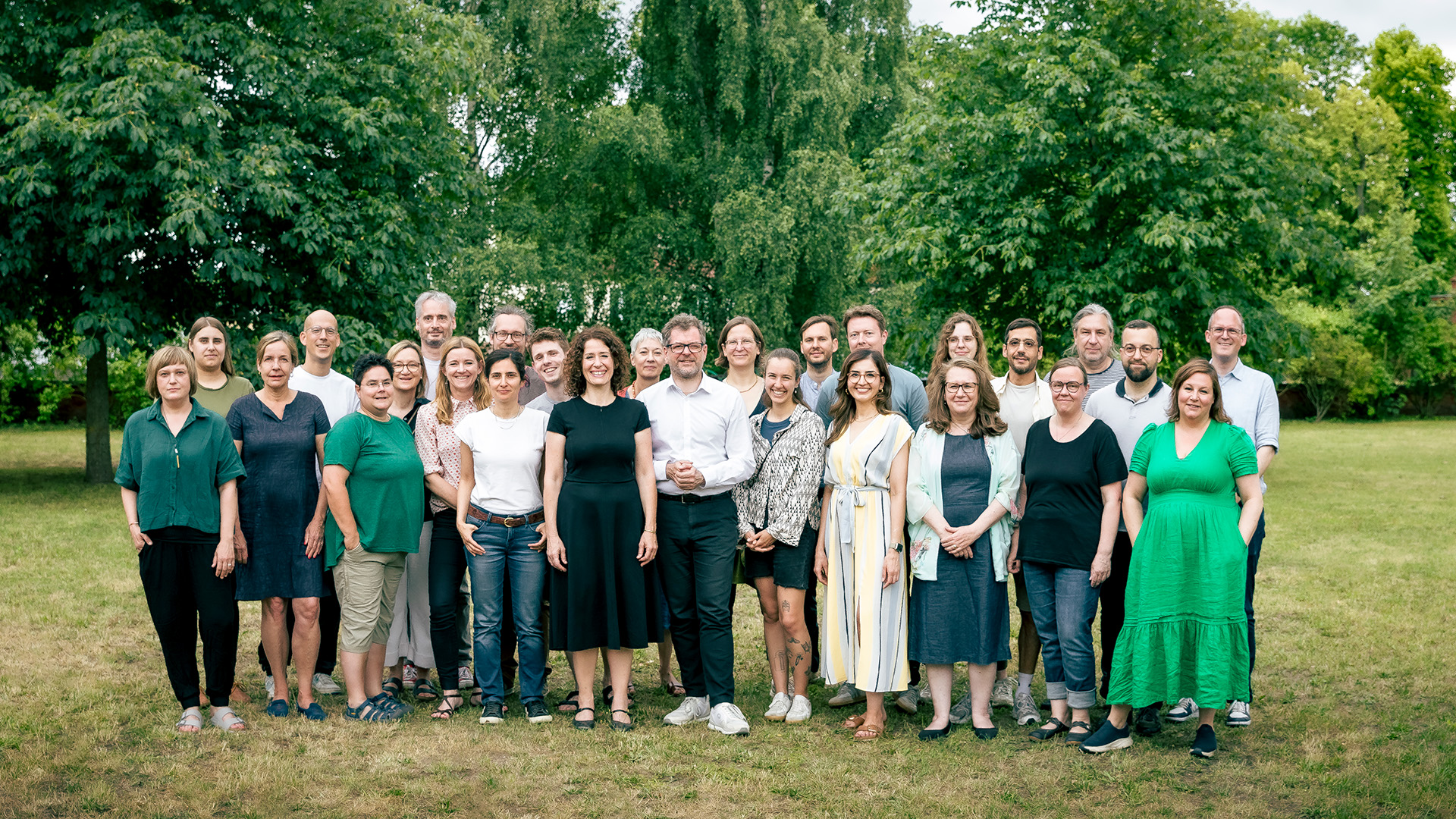 Ein Gruppenfoto von Abgeordneten der Grünen Fraktion aus dem Berliner Abgeordnetenhaus, die Personen stehen zusammen vor einem Hintergrund mit Bäumen.