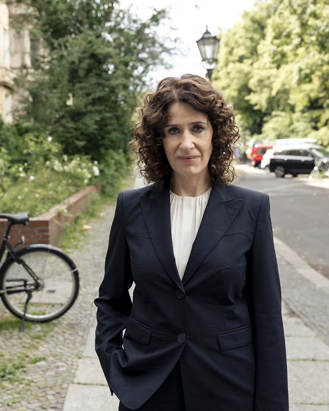 Bettina Jarasch, Co-Spitzenkandidatin für die Berlin-Wahl, steht auf einer Straße, im Hintergrund ist es grün, sie schaut in die Kamera.  Foto: Vincent Villwock