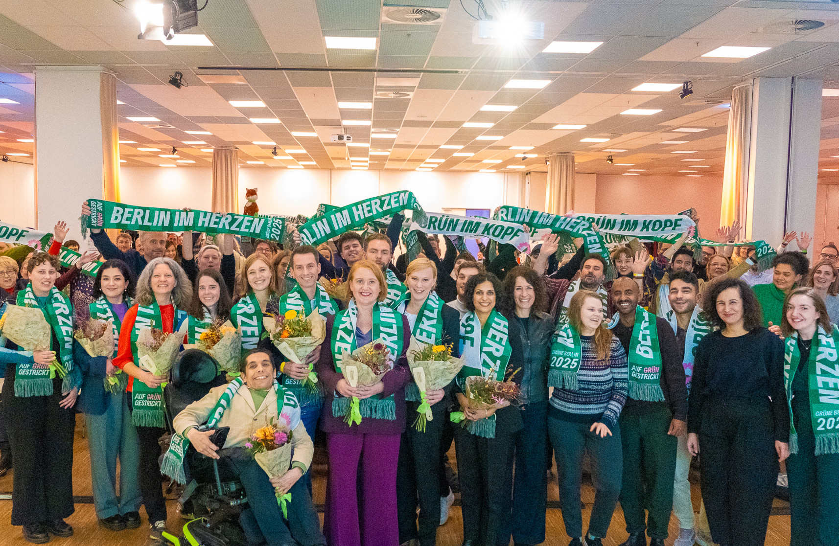 Gruppenfoto von der Landesdelegiertenkonferenz, im Vordergrund die 14 Kandidierenden auf der Landesliste zur Bundestagswahl. Alle tragen grüne Schals. Foto: Bündnis 90/Die Grünen Berlin