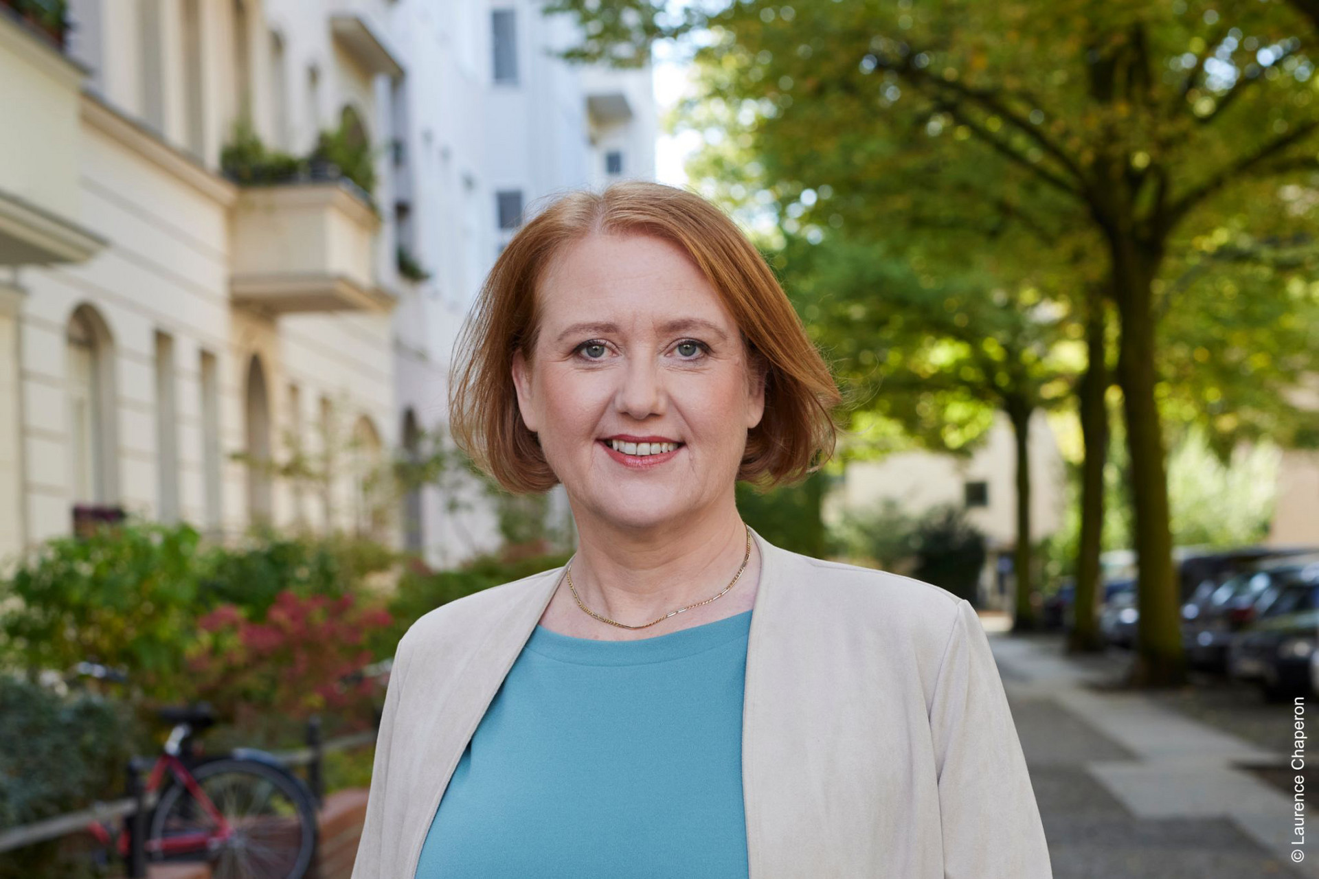 Ein Portraifoto der Bundestagsabgeordneten Lisa Paus, sie trägt ein blaues T-Shirt und einen hellen Blazer und lächelt in die Kamera. Sie steht draußen auf einem Gehweg. Foto: Laurence Chaperon