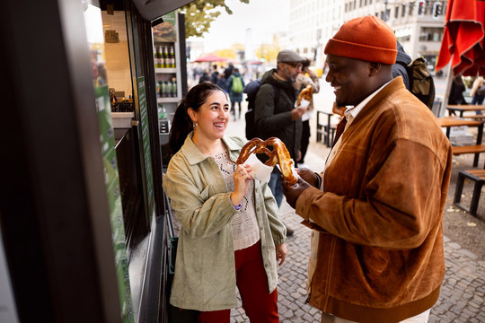 Zwei Personen stehen an einem Imbiss und lachen sich an Foto: GettyImages/SrdjanPav
