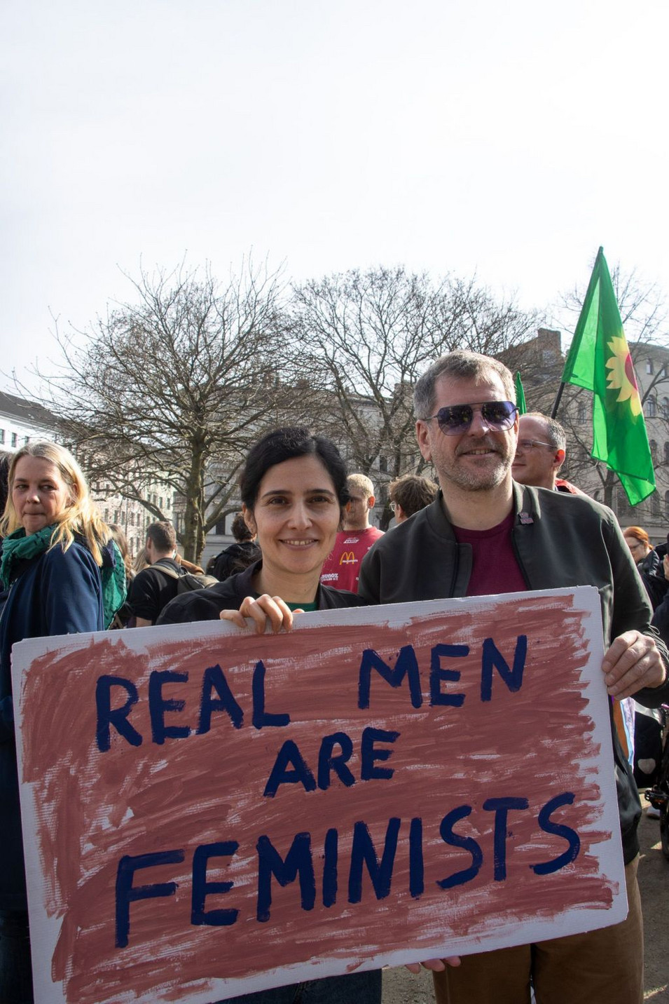 Bahar Haghanipour und Werner Graf halten ein Schild hoch, auf diesem steht: Real men are feminists.