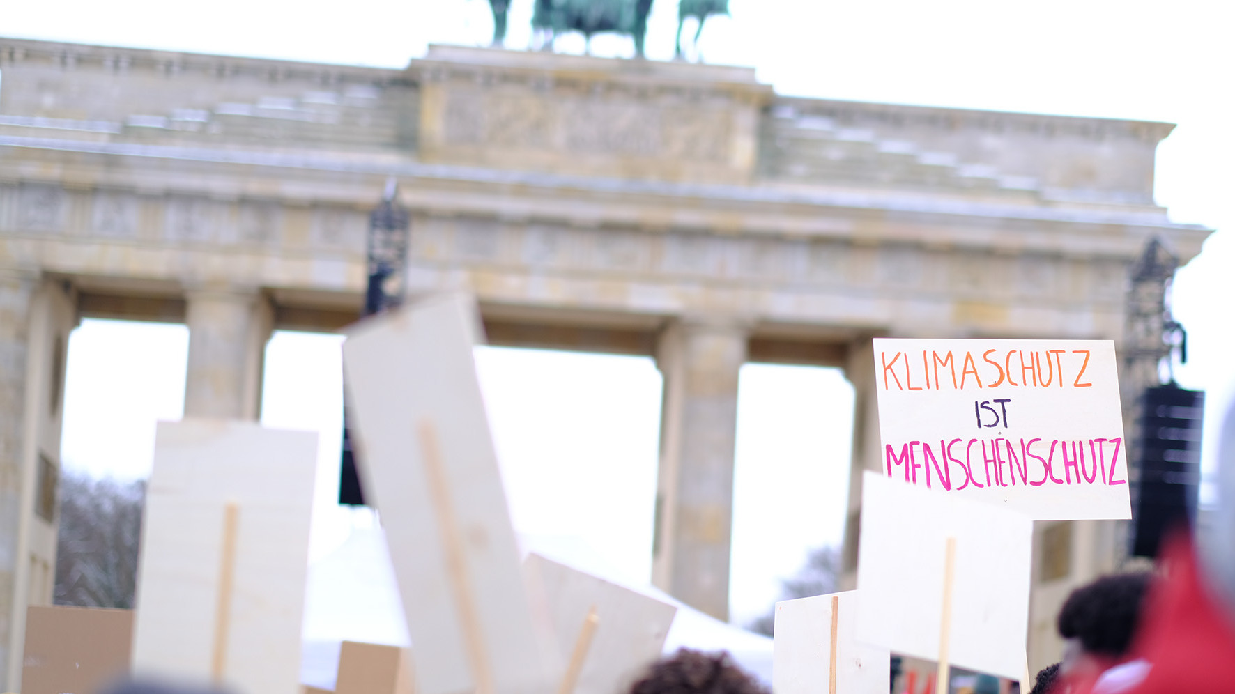 Viele Personen drängen sich auf einer Demo vor dem Brandenburger Tor, man sieht Plakate mit Aufschriften wie "Klimaschutz ist Menschenschutz" 
