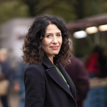 Portraitfoto von Bettina Jarasch, Spitzenkandidatin für Bündnis 90/Die Grünen Berlin. Bettina steht seitlich und blickt direkt in die Kamera. Im Hintergrund unscharf eine Marktsituation.