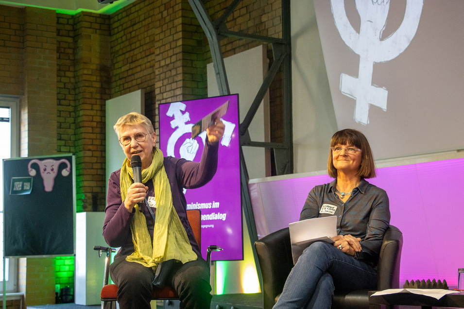 Zwei Personen sitzen auf einer Bühne nebeneinander