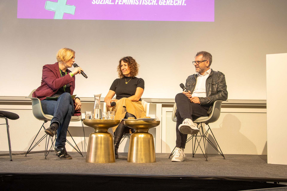 Nina Stahr, Landesvorsitzende von Bündnis 90/Die Grünen Berlin sitzt neben Bettina Jarasch und Werner Graf auf einer Bühne und moderiert ein Gespräch. 