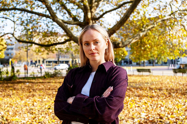 Ein Portraitfoto von Jette Gunkel. Sie steht vor Bäumen mit herbstlichem Laub und verschränkt die Arme.