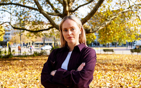 Ein Portraitfoto von Jette Gunkel. Sie steht vor Bäumen mit herbstlichem Laub und verschränkt die Arme.