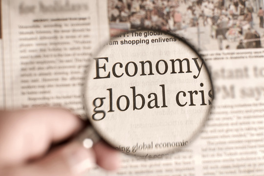 Blick durch eine Lupe auf einen Zeitungsartikel mit der Überschrift Globale Wirtschaftskrise fotosipsak via Getty Images