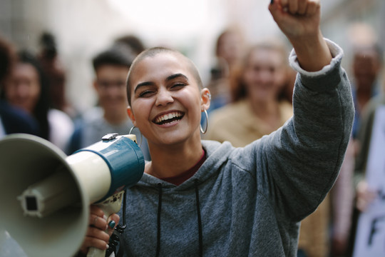 Eine junge Person mit Megafon steht lachend auf einer Demonstration © Getty Images
