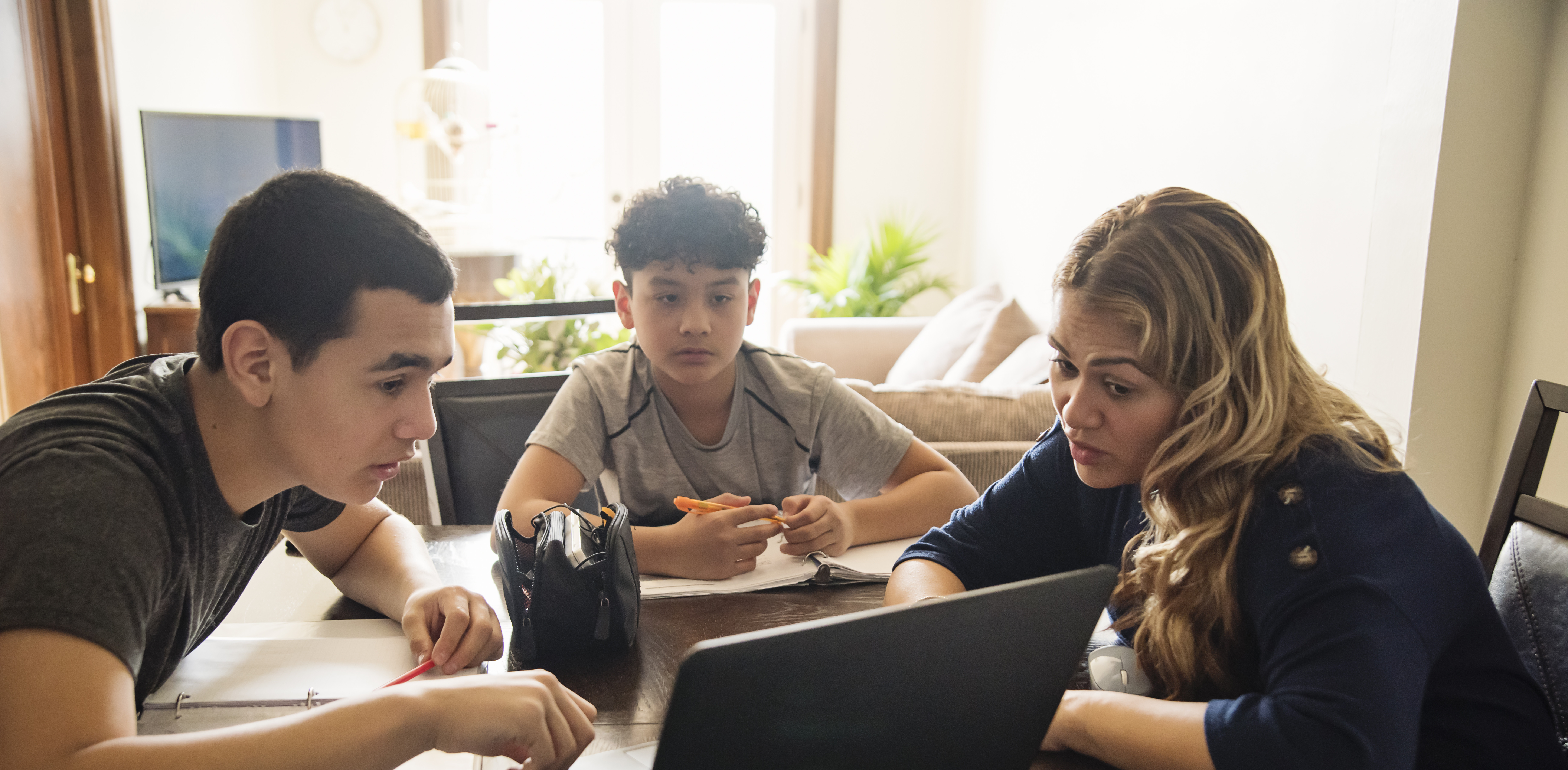 Frau mit zwei Kindern sitzen gemeinsam zu Hause vor einem Laptop Martine Doucet via Getty Images