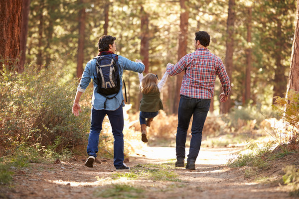 Zwei Männer lassen ein Kind zwischen sich an den Armen durch die Luft fliegen während sie im Wald spazieren gehen Getty