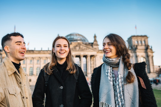 Drei junge Menschen stehen lachend bei gutem Wetter vor dem Reichtsagsgebäude golero via Getty Images
