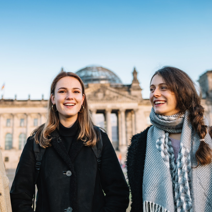 Drei junge Menschen stehen lachend bei gutem Wetter vor dem Reichtsagsgebäude golero via Getty Images