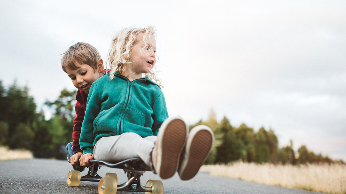 Zwei Kinder sitzen hintereinander auf einem Skateboard und rollen eine Straße entlang Foto: GettyImages/Ryan J. Lane