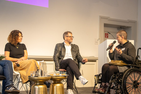 Bettina Jarasch, Werner Graf und eine teilnehmende Person der FLINTA-Konferenz sprechen auf der Bühne miteinander.