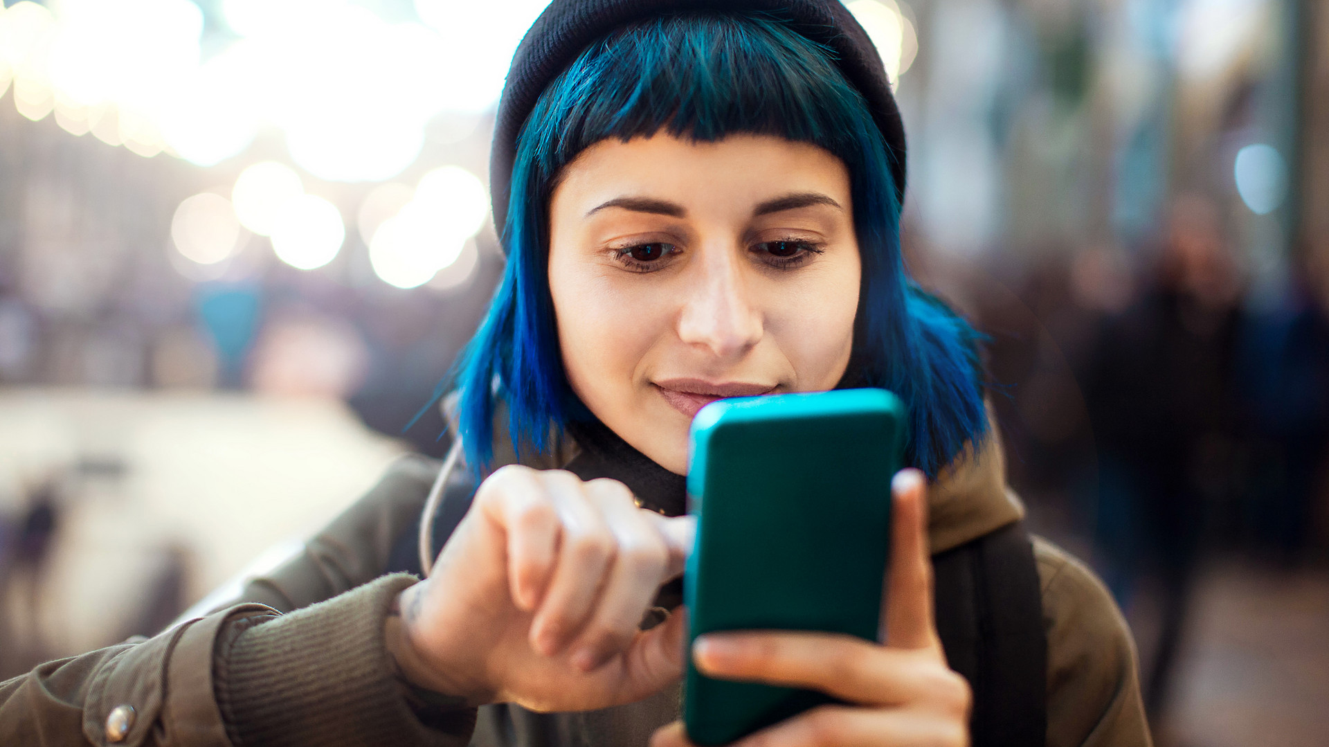 Eine junge Frau mit blauen Haaren schaut auf ihr Smartphone und tippt auf dessen Bildschirm. Marco Piunti via Getty Images