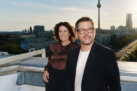 Bettina Jarasch und Werner Graf stehen auf einem Hausdach nebeneinander und lächeln. Im Hintergrund die Berliner Skyline. Foto: Bündnis 90/Die Grünen Berlin
