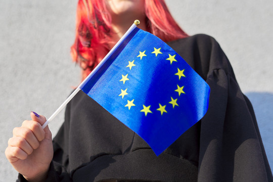 Eine junge Frau, deren Gesicht nicht erkennbar ist, hält eine kleine Europaflagge in der Hand.