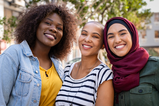 Drei Women of Colour, davon eine Muslima, lächeln in die Kamera Getty